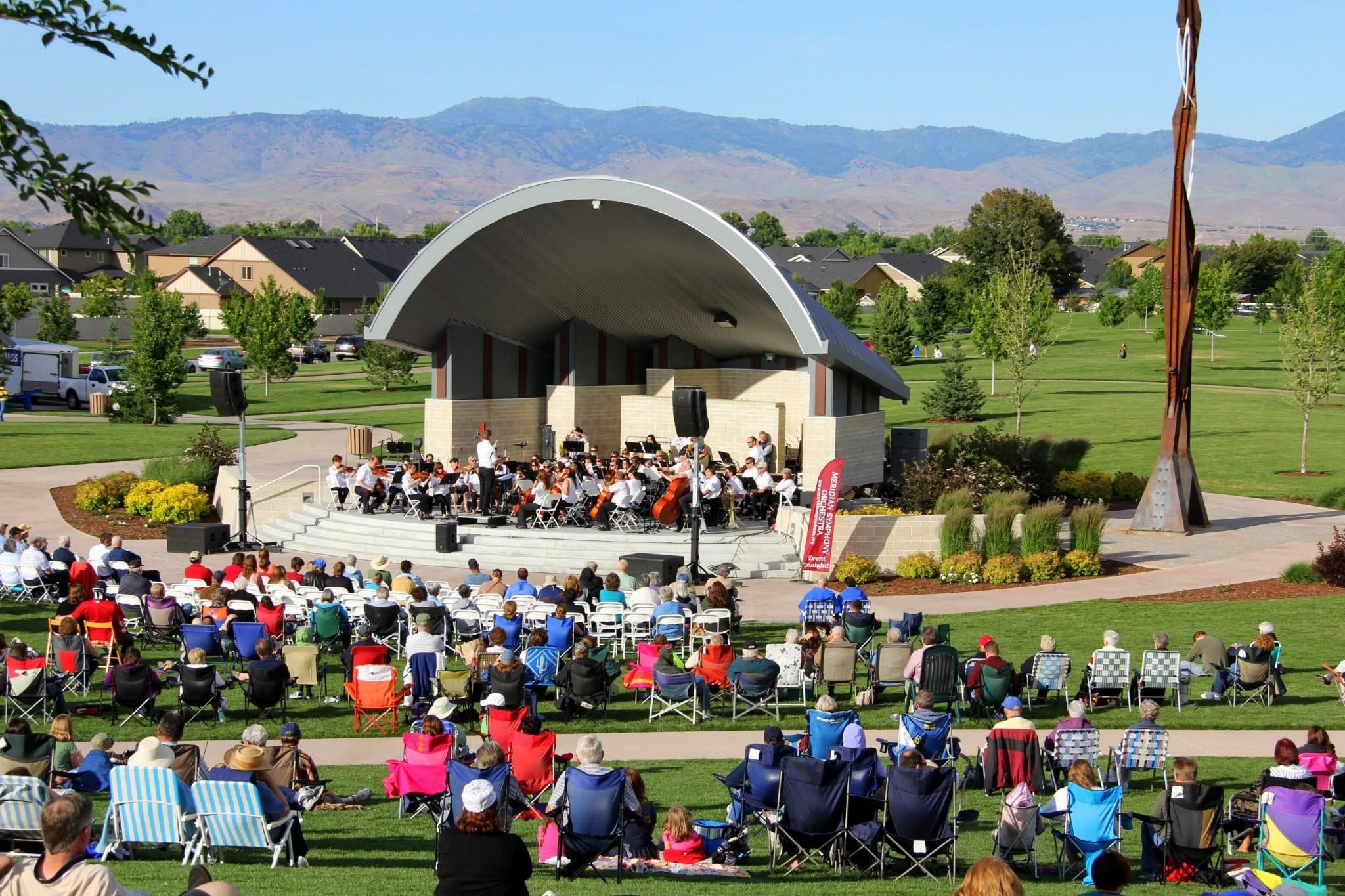Ochestra playing at Gene Kleiner Bandshell with people in lawn chairs listening.